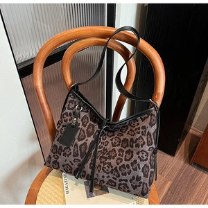Détail d'un sac cabas léopard avec bordure en cuir noir accroché à une chaise
