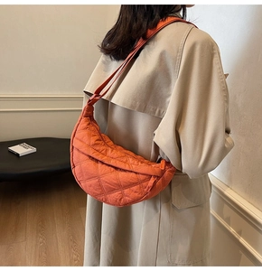 Close-up of orange quilted crescent bag with diamond stitching and adjustable strap