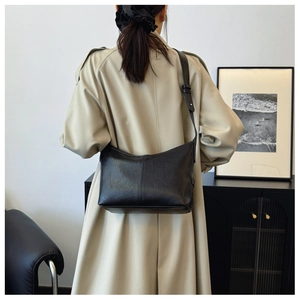 Model wearing black textured leather underarm bag with beige coat in a minimalist interior