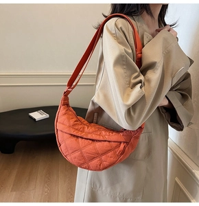 Detail of orange quilted crescent bag with adjustable shoulder strap and zipper closure