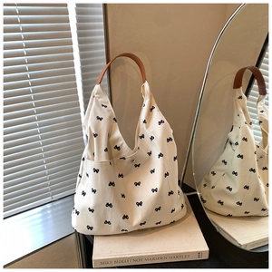 Close-up of cream canvas tote bag with black bow embroidery and brown leather strap