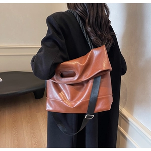 Detail of a brown leather tote with a black woven rope handle and wide shoulder strap
