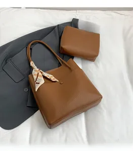 Detail view of brown lychee grain leather tote bag with decorative silk scarf on white linen
