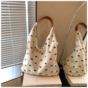 Detail of off-white canvas tote bag featuring black bow patterns and brown leather handles