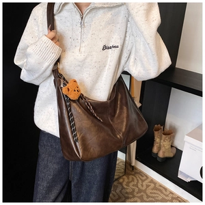 Detail view of deep brown leather shoulder bag with plush bear charm and woven rope accent