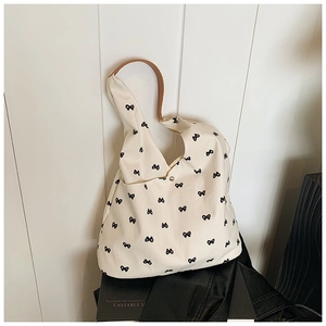 Close-up of canvas tote bag with black bow patterns and brown leather handle