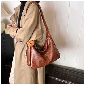 Detail of a brown leather hobo bag featuring a cute teddy bear charm and checkered strap