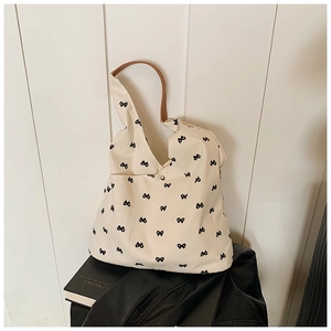 Detail of canvas tote featuring bow patterns, leather handle, and metal snap closure