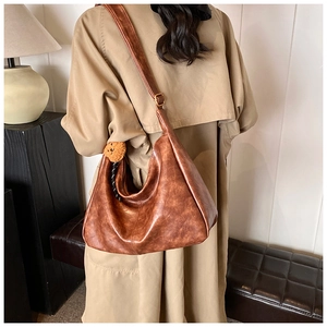 Detailed view of brown hobo crossbody bag with a plush bear charm on a trench coat