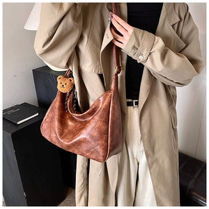 Close-up of vintage brown hobo bag featuring a cute plush bear charm on the shoulder strap
