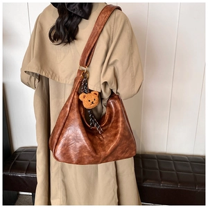Detail of retro brown hobo bag with plush bear charm worn by a model in a trench coat
