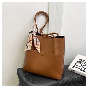 Detail of caramel leather bucket bag with litchi texture and printed silk scarf on handle