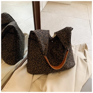 Close-up of leopard print tote bag with brown leather strap on a beige trench coat