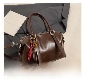 Detail van donkerbruine baguette tas met gevlochten touw en sleutelhanger decoratie