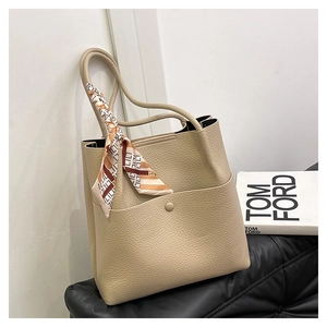 Close-up of beige lychee texture leather bucket bag with decorative silk scarf on handle