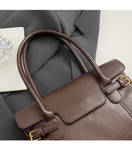 Close-up of brown leather tote bag with gold logo on professional grey suit backdrop