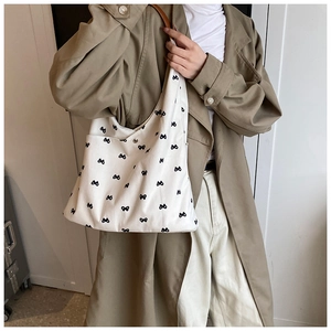 Close-up of white canvas tote bag with black bow print and leather shoulder strap