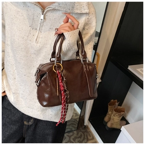 Sac à main vintage marron avec pendentif tressé rouge et détails dorés porté par modèle