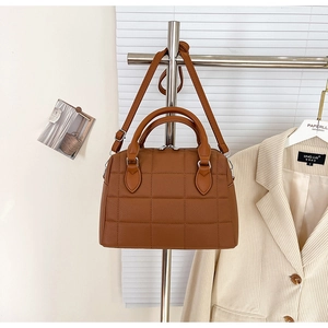 Close-up of caramel brown quilted boston bag with lychee texture and metallic hardware