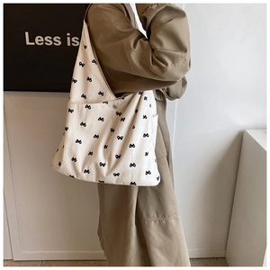 Detail view of large white hobo bag with black bow prints on a beige trench coat