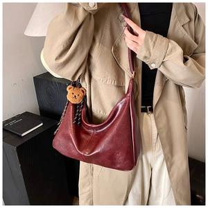 Detail view of burgundy semi-circle crossbody bag with a cute plush bear pendant accessory