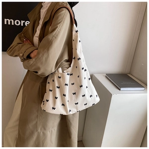 Detail of white canvas tote bag with black bow pattern and brown leather shoulder strap