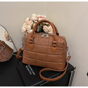 Detail of caramel quilted Boston bag with litchi texture on a stylish display box
