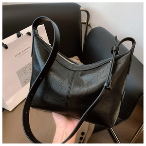 Detail of black pleated faux leather hobo bag with adjustable strap on a vintage chair