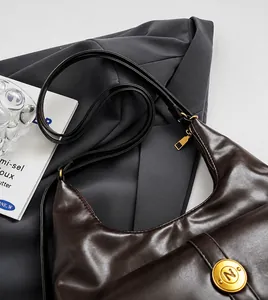 Dettaglio tracolla regolabile e fibbia dorata su borsa a mezzaluna in pelle marrone