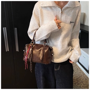 Détail d'un sac Boston marron foncé brillant avec breloque porté par un mannequin