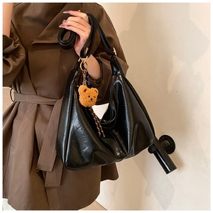 Detail of black glossy Hobo bag with brown teddy bear charm and wide shoulder strap