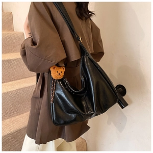 Detail of large black hobo bag in glossy leather with cute brown teddy bear keychain