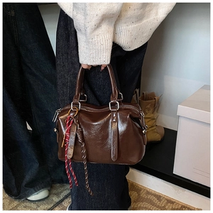 Détail du sac Boston en cuir verni marron foncé avec breloque en corde tressée