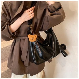 Detail of black glossy crescent bag with wide strap and cute brown teddy bear charm