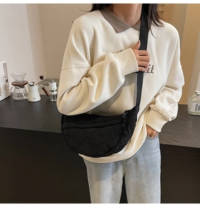 Close-up of black quilted dumpling shoulder bag worn by model in a modern cafe setting