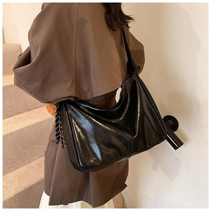 Detail of black glossy hobo bag with woven fringe accents on model's shoulder