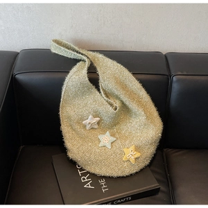 Detailaufnahme der Stricktextur einer goldenen Schultertasche mit Sternanhängern auf Sofa