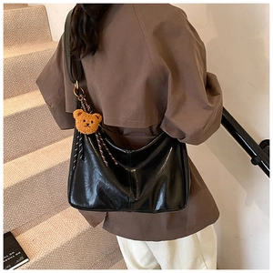 Detail of a black glossy leather shoulder bag featuring a cute plush bear charm