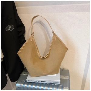 Detail der kamelfarbenen Wildleder-Tote-Bag mit V-Schnitt auf weißen Büchern und Koffer