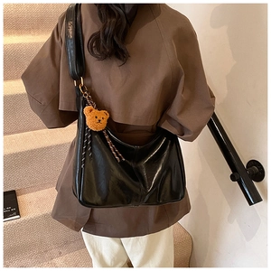 Close-up of black glossy crescent bag with wide shoulder strap and brown plush bear charm