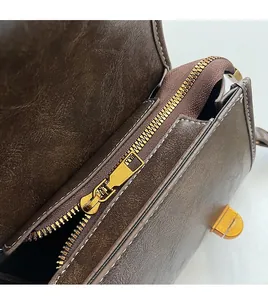 Détail d'une fermeture éclair dorée et texture cuir ciré sur un sac marron vintage