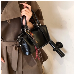 Détail d'un sac Boston en cuir verni noir avec des pendentifs en corde tressée