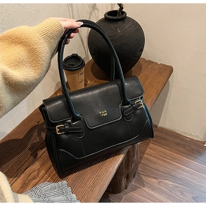 Detail of a black leather underarm bag featuring a gold brand logo and square buckle
