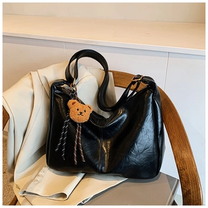 Detail of black leather shoulder bag with fine texture and a brown plush bear charm
