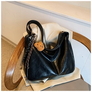 Detail of black faux leather tote with plush bear and striped scarf on beige blazer