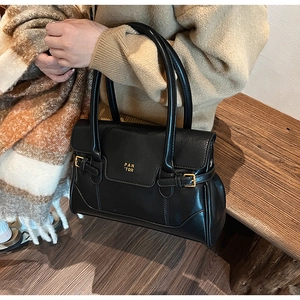 Detailed view of black vintage leather tote bag with gold logo on a model in autumn setting