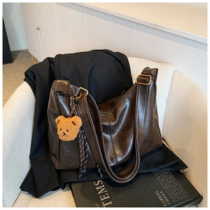 Detail of dark brown retro crossbody bag with plush bear charm on white sofa