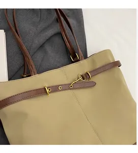 Detail of khaki nylon tote bag with brown leather handles and gold buckle decorations
