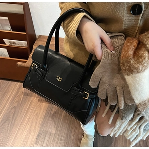 Close-up of black leather tote bag with vintage flap and gold buckles for autumn style