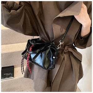 Detail van zwarte laklederen crossbodytas met gevlochten touw en glanzende afwerking